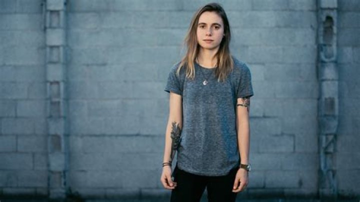 Julien Baker Is Wearing Dark Ash And Black Dress Standing In White Wall